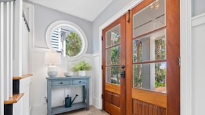 A hallway with a wooden door, a round mirror, a blue console table with a lamp, and a potted plant.