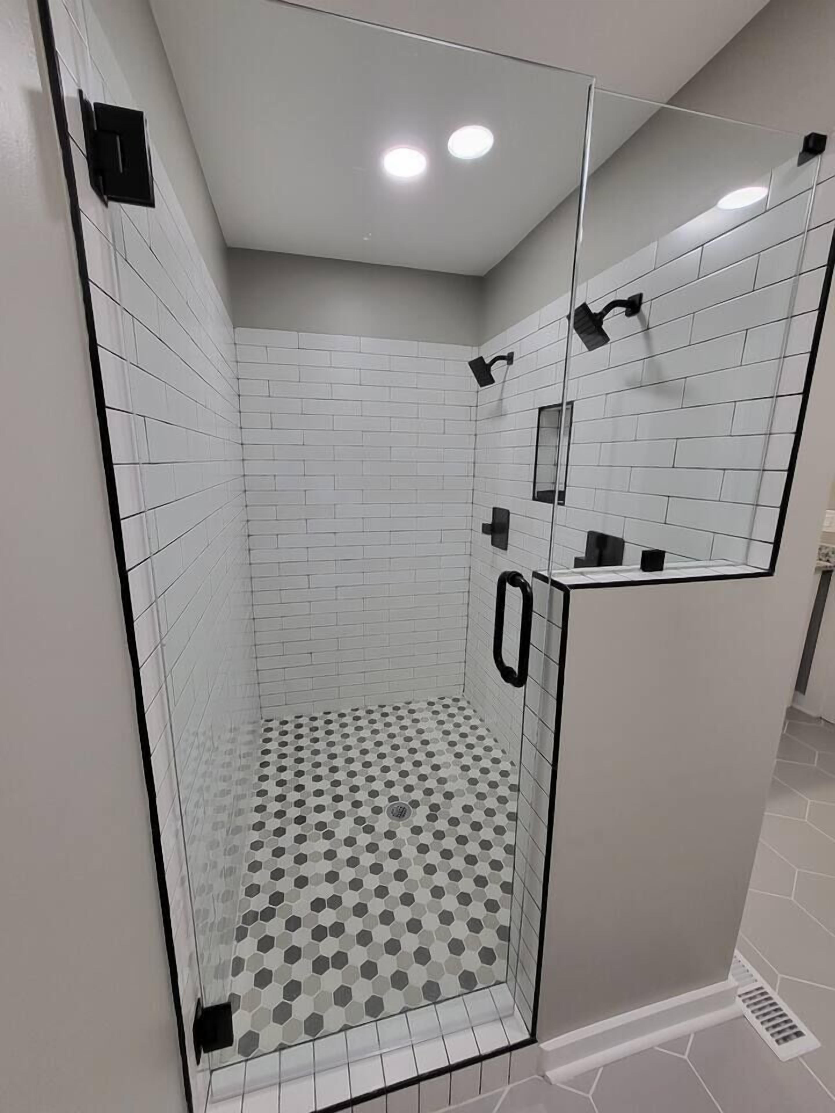 Una ducha moderna con paredes de azulejos blancos, piso de diseño hexagonal y separador de vidrio.