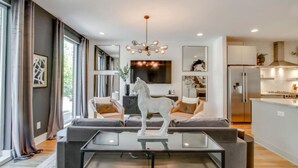 A modern living room with a glass coffee table, a sofa, and a mounted TV. - Midtown Skyline Retreat | Rooftop Deck | Game Room (Nashville)