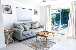 Una sala de estar moderna con un sofá gris, una mesa de centro de madera y un ventanal con cortinas.