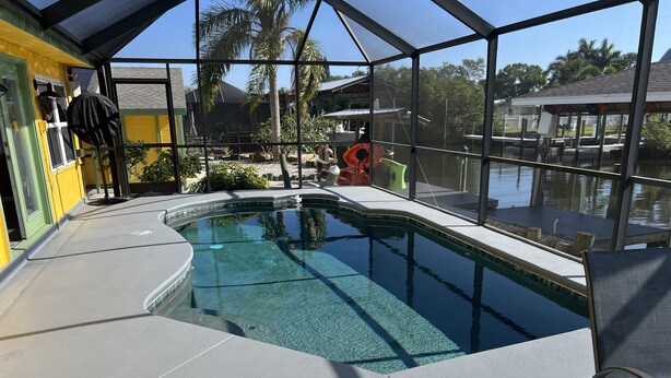 An indoor swimming pool with clear water, surrounded by a covered area with large windows. - Florida waterfront home with pool and use of kayaks (Ruskin)
