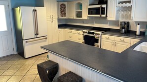A kitchen with white cabinets, a black countertop, and a tiled floor. - Florida waterfront home with pool and use of kayaks (Ruskin)
