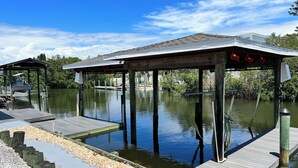 A dock extending into a calm body of water with a covered structure at the end. - Florida waterfront home with pool and use of kayaks (Ruskin)