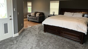 A bedroom with a large bed, a dark wooden headboard, a grey sofa with patterned cushions, and a grey carpet. - Florida waterfront home with pool and use of kayaks (Ruskin)