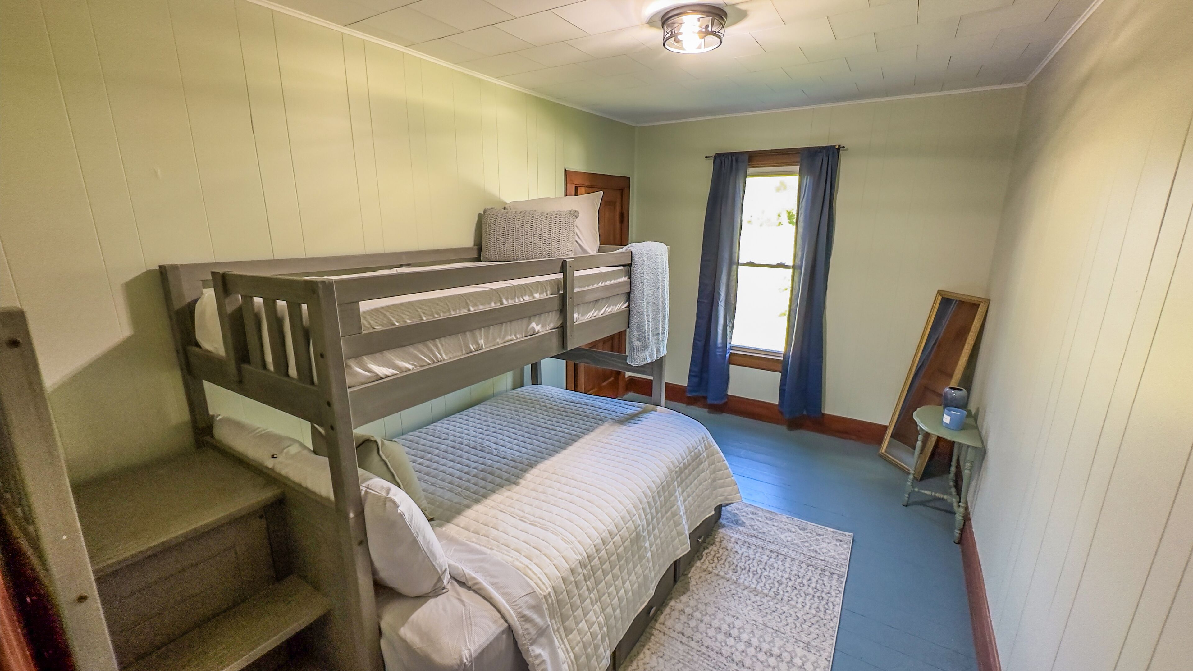 A bunk bed room with a window, a small table, and a mirror.