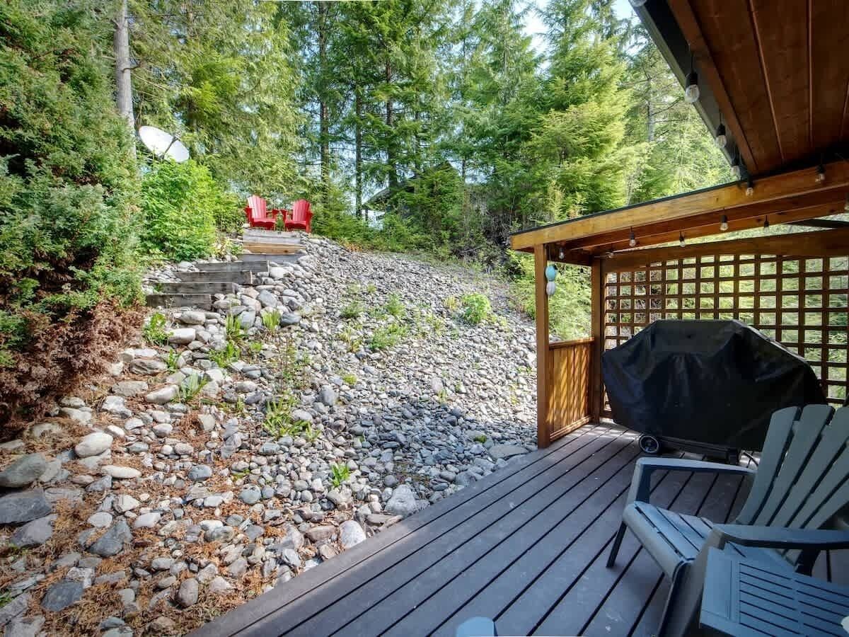 Una terraza de madera con una parrilla y sillones Adirondack, rodeada de un paisaje rocoso y árboles frondosos.