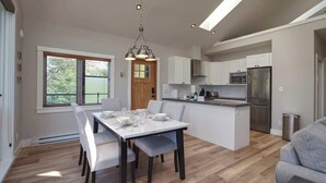 Eine moderne Küche mit weißen Schränken, einem Edelstahl-Kühlschrank und einem Essbereich mit weißem Tisch und Stühlen.
