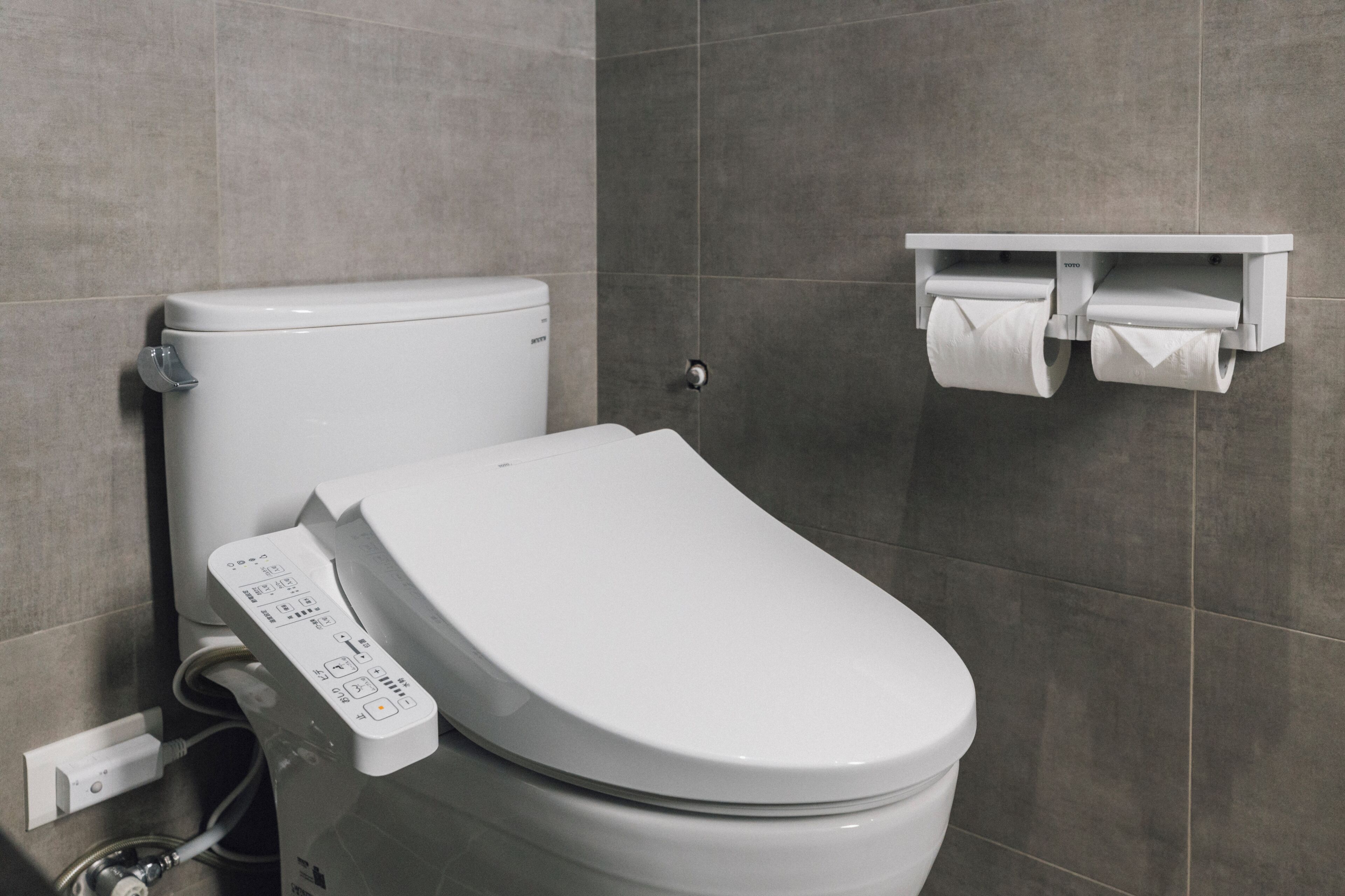 Un baño moderno con inodoro, dispensador de papel higiénico montado en la pared y panel de control visible en el inodoro.