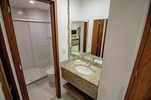 A bathroom with a white toilet, a sink with a mirror, and a shower area. - RIVIERA PARK - JC TEMPORADA (Caldas Novas)