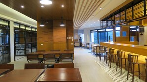 A modern dining area with wooden tables and chairs, a bar with stools, and large windows providing natural light. - Alvea Hotel Baguio  (Baguio)