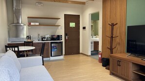 A compact living space with a kitchenette, a sofa, a TV, and a wooden accent wall. - Alvea Hotel Baguio  (Baguio)