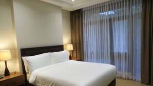 A hotel room with a large bed, two bedside tables with lamps, and a window with sheer curtains. - Alvea Hotel Baguio  (Baguio)