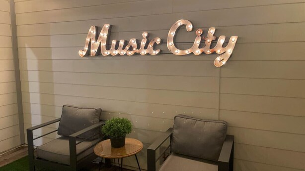 A seating area with two chairs and a small table, a potted plant, and a wall sign that reads "Music City". - Stylish Rooftop Haven | Sleeps 12 Comfortably (Nashville)