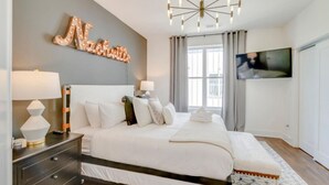 A modern bedroom with a bed, bedside lamps, a TV, and a decorative wall piece. - Stylish Rooftop Haven | Sleeps 12 Comfortably (Nashville)