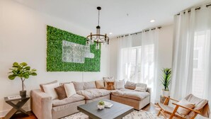 A modern living room with a sectional sofa, a coffee table, and a green wall with a sign. - Stylish Rooftop Haven | Sleeps 12 Comfortably (Nashville)