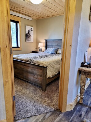 Een slaapkamer met een houten bed, een nachtkastje met een lamp, een lijst met een foto aan de muur en een raam met zonwering.