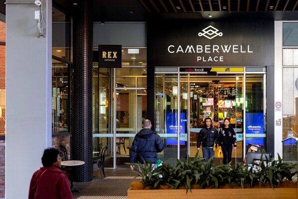 The exterior of Camberwell Place with a Rex Espresso sign, glass doors, and a visible officeworks sign.