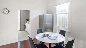 Una cocina moderna con un refrigerador de acero inoxidable, una mesa redonda de mármol con cuatro sillas, un reloj y una ventana con persianas.