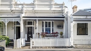 Una casa blanca de dos pisos con balcón, cerca de piquetes y un pequeño jardín.