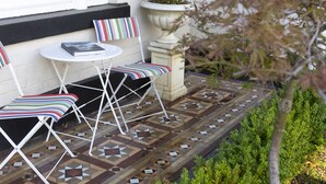 Un patio con una mesa blanca y dos sillas a rayas, una planta en maceta y un suelo estampado.