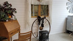 Une pièce comprenant un meuble en bois, une chaise, une grande roue en bois et un petit poêle noir.