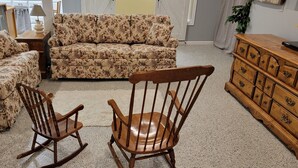 Un salon avec un canapé à motifs floraux, un fauteuil à bascule et une commode en bois.