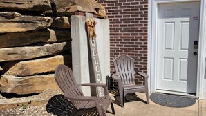 Deux fauteuils Adirondack sont placés à l’extérieur d’un bâtiment doté d’un mur en pierre et d’une porte blanche.