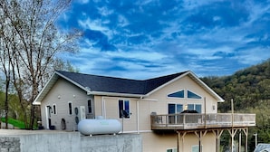 A two-story house with a balcony, a large water tank, and a stone retaining wall. - River Run Ridge- HOT TUB- sleeps 14 (Lynxville)