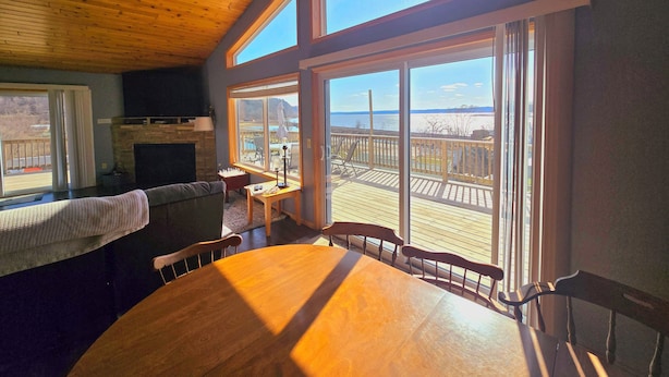 A cozy room with a wooden ceiling, large windows, a fireplace, and a dining area with a table and chairs. - River Run Ridge- HOT TUB- sleeps 14 (Lynxville)