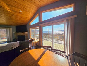 Una habitación acogedora con techo de madera, ventanas amplias, chimenea y zona de comedor con mesa y sillas.