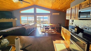 A spacious kitchen with wooden cabinets, a microwave, and an oven. There is a dining area with a table and chairs, and a large window offering a view of the outdoors. - River Run Ridge- HOT TUB- sleeps 14 (Lynxville)