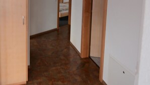 A hallway with wooden doors and a patterned floor, leading to a bedroom with a bed and a mirror. - Bergfreude 06 by Interhome (Saas-Fee)