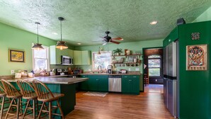A kitchen with green cabinets, wooden bar stools, a central island, and a refrigerator. -     Peaceful Mountain Retreat: Private Creek, Fireflies & Family Fun (Sparta)