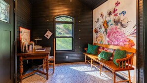 A cozy room with a wooden bench, a desk with a lamp, and a large floral painting on the wall. -     Peaceful Mountain Retreat: Private Creek, Fireflies & Family Fun (Sparta)