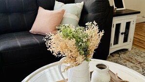 A living room with a white coffee table, a vase with dried flowers, and a small white cabinet with a lamp. - Remodeled, cozy, vintage charmer (Albany)