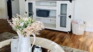 A living room with a white cabinet, a flat-screen TV mounted above it, and a decorative vase on a wooden tray. - Remodeled, cozy, vintage charmer (Albany)