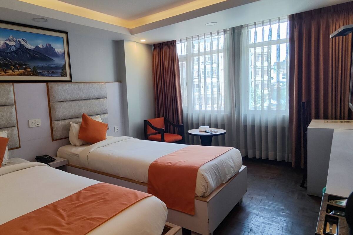 A hotel room with two beds, a desk, a chair, a TV, and a painting on the wall.