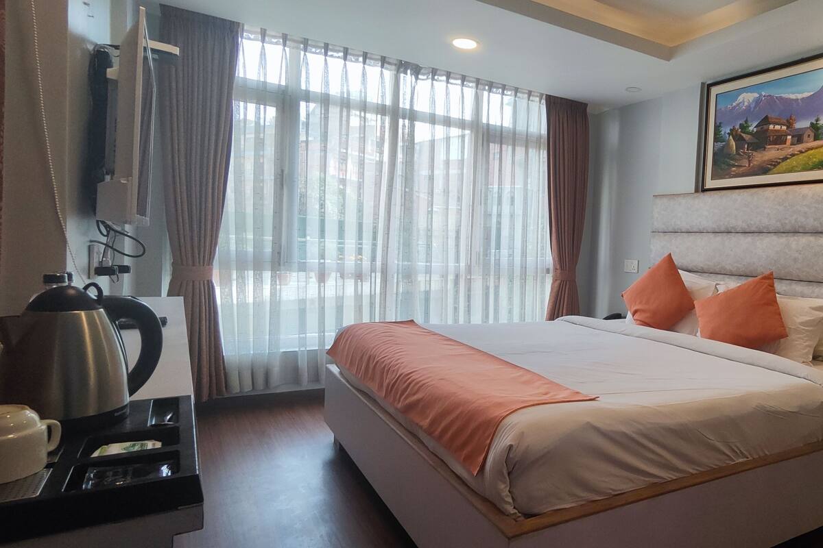 A hotel room with a large bed, a painting on the wall, and a window with curtains.