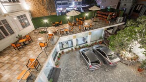 Una terraza en la azotea con mobiliario exterior, un coche estacionado al frente y vistas de los edificios circundantes.