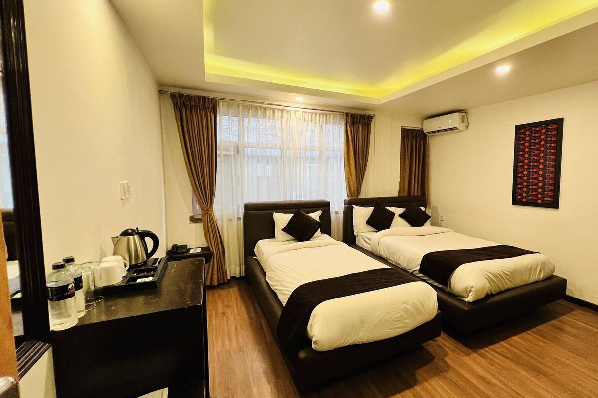 A hotel room with two beds, a desk with a kettle, a coffee maker, and a framed picture on the wall.