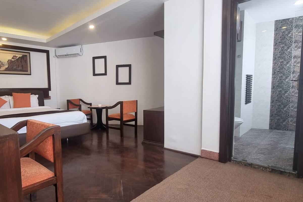 A hotel room with a bed, two chairs, a small table, and a painting on the wall.