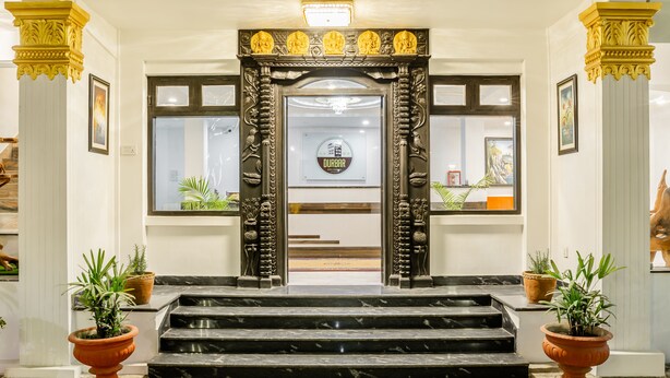 Una entrada imponente con columnas ornamentales, una escalinata de mármol y plantas en macetas.