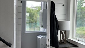 Une petite pièce avec une fenêtre, un lave-linge, un étendoir et une chaise.