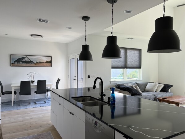 A modern kitchen with a central island, pendant lighting, and a dining area with chairs and a table.