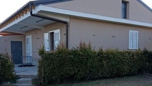 A modern two-story house with a flat roof, a covered porch, and a small front yard with a hedge.