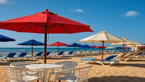 A beach with rows of sun loungers and umbrellas, a table with chairs, and the ocean in the background. - Beachfront Chalet in Porto Said Egypt  Perfect Getaw (Port Said Governorate)