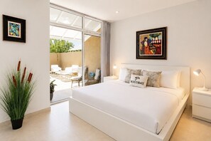 Une chambre à coucher moderne avec un grand lit, une porte vitrée donnant sur un patio et un tableau encadré au-dessus du lit.