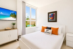 Une chambre d’hôtel avec un lit, une télévision, une fenêtre donnant sur une piscine et un meuble avec une plante.