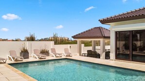 Une piscine avec des chaises longues, un belvédère et un bâtiment doté de grandes fenêtres.