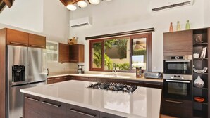 Une cuisine moderne dotée d’un grand îlot central, d’appareils électroménagers en acier inoxydable et de meubles de rangement en bois foncé.